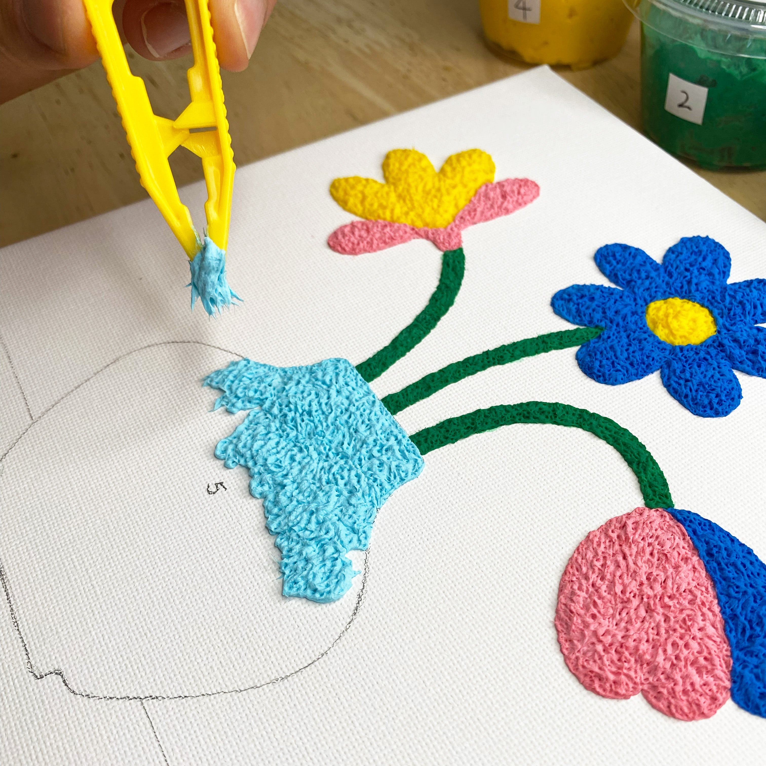 Colorful paper-paste flowers on fabric with a hand using tweezers.